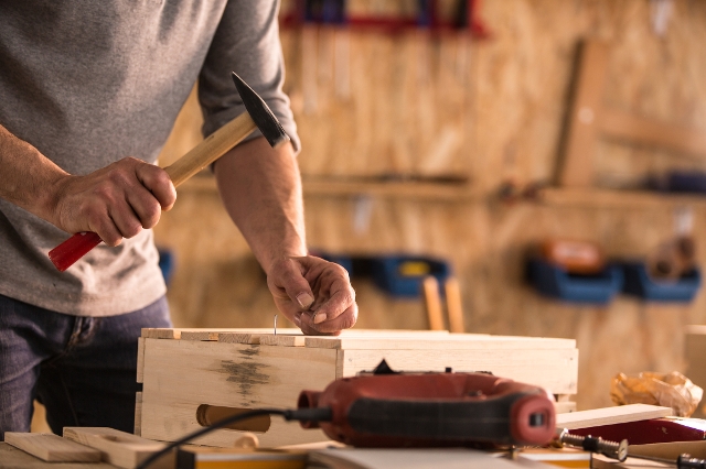 Mann schlägt mit einem Hammer einen Nagel in ein Holzbrett ein.