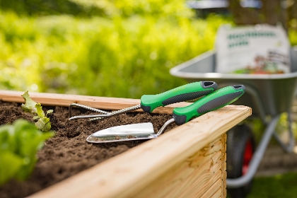 Gartenhandwerkzeug liegt am Rand eines Hochbeetes