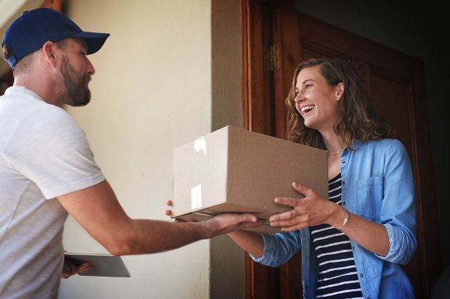 Lieferservice übergibt Einkauf aus Lagerhaus Onlineshop an Dame, die sich Paket nach Hause liefern lassen hat.