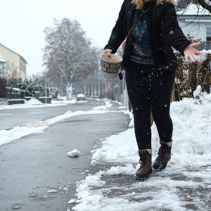 Salz streuen im Winter: Frau streut mit Streusalz