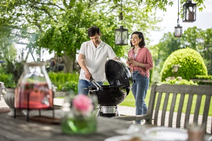 Sommerliche Grillszene im Garten: Ein Mann grillt am Kugelgrill, eine Frau steht neben ihm